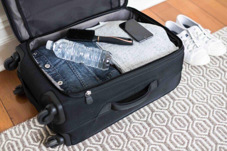 Small overnight black suitcase with wheels packed with clothes and essentials lying on timber floorboards at home ready to go